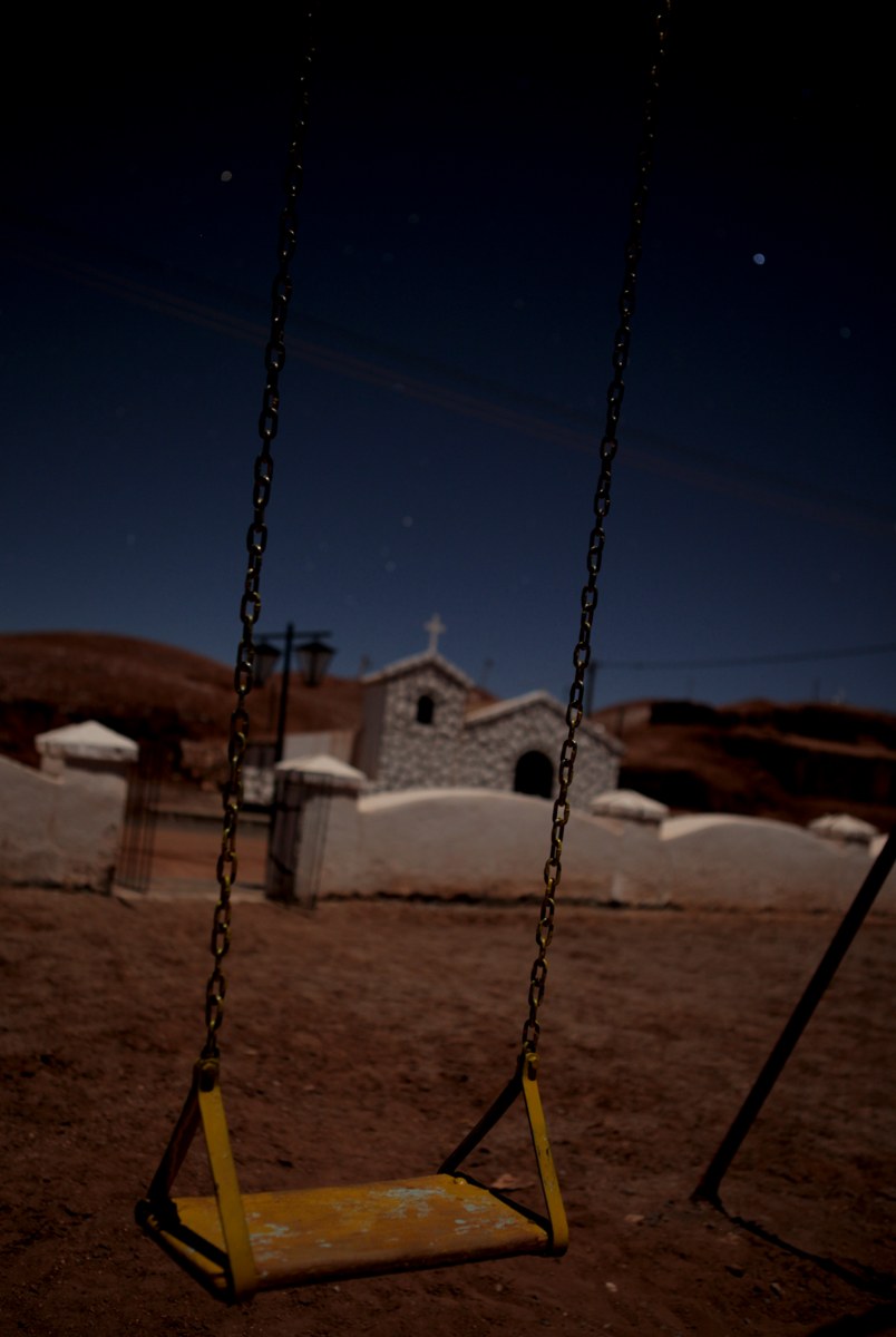 Hamaca vacía frente a una iglesia de noche, con las cadenas en primer plano